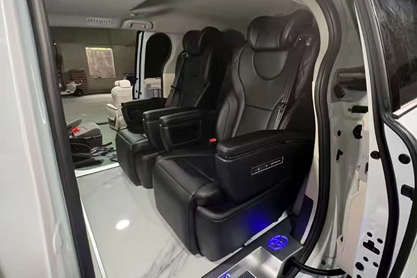 Pair of black leather captain seats mounted in vehicle, with armrest control panel and ambient light