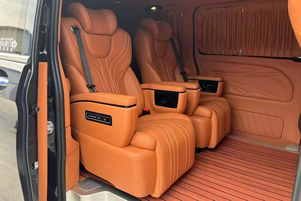 Pair of orange leather captain seats installed inside MPV, armrest control panel and vertical stitching design